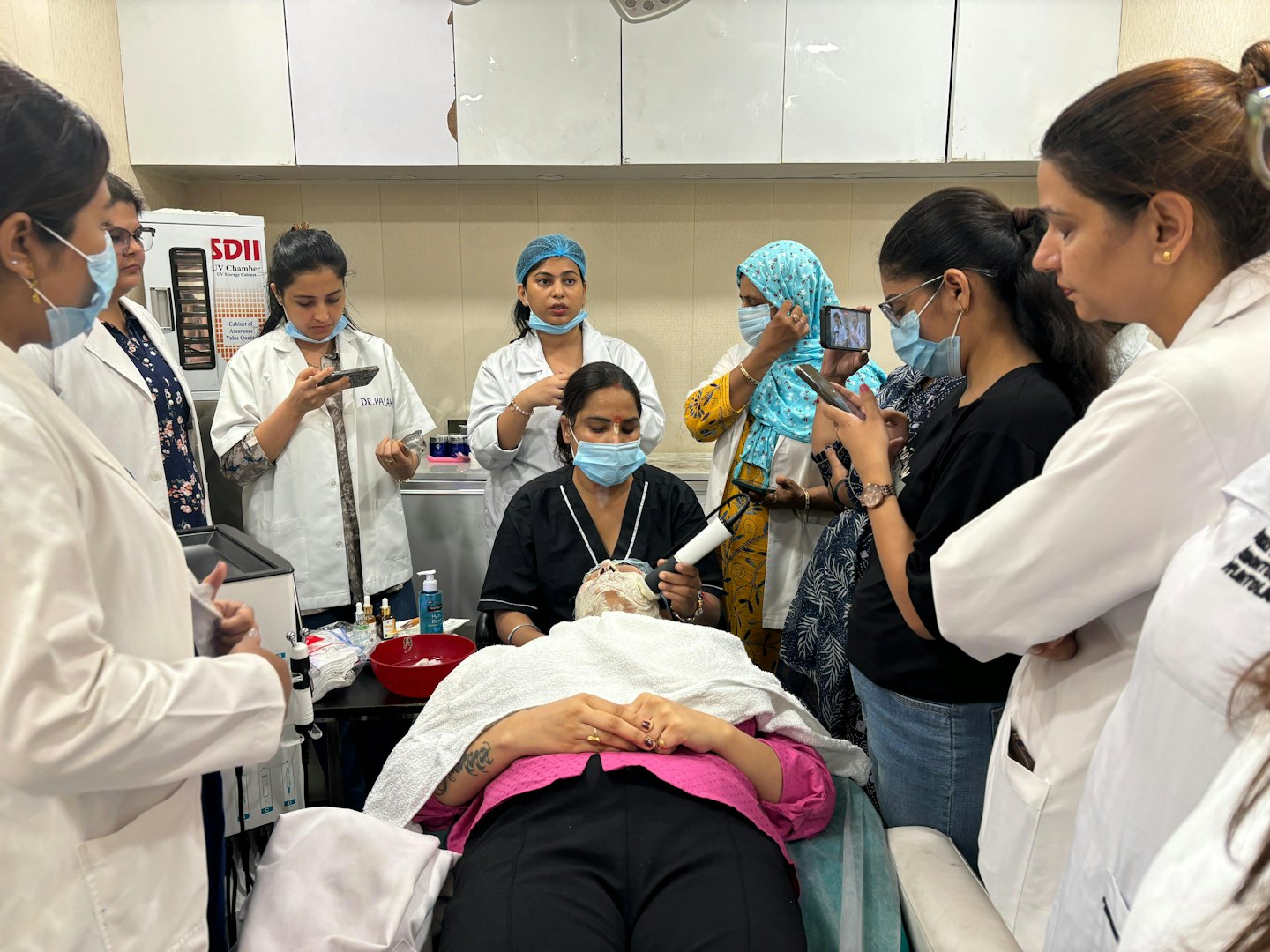 Women observe skincare professional demonstrating treatment in clinic.